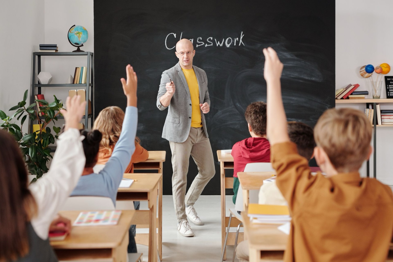 Docent voor de klas terwijl leerlingen hun hand opsteken, beeld bij DISC voor docenten