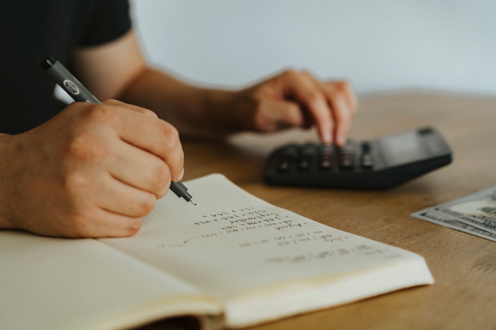 Handen die een tariefberekening maken in een notitieboek met rekenmachine, passend bij het bepalen van je uurtarief als DISC-trainer