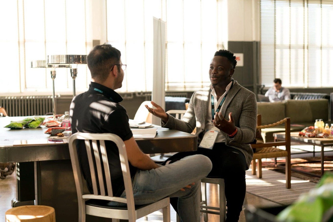Coach in gesprek met een coachee aan tafel in een lichte werkruimte, over de eigen stijl als coach