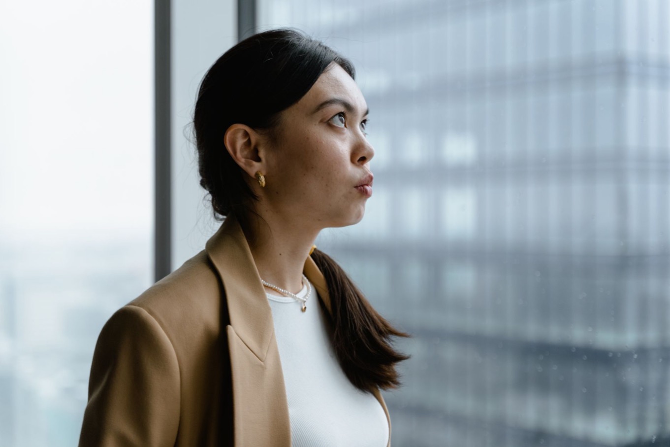 Een vrouw in een bruine blazer kijkt peinzend uit het raam van een kantoor, als beeld voor nadenken over je eigen aandeel in een conflict