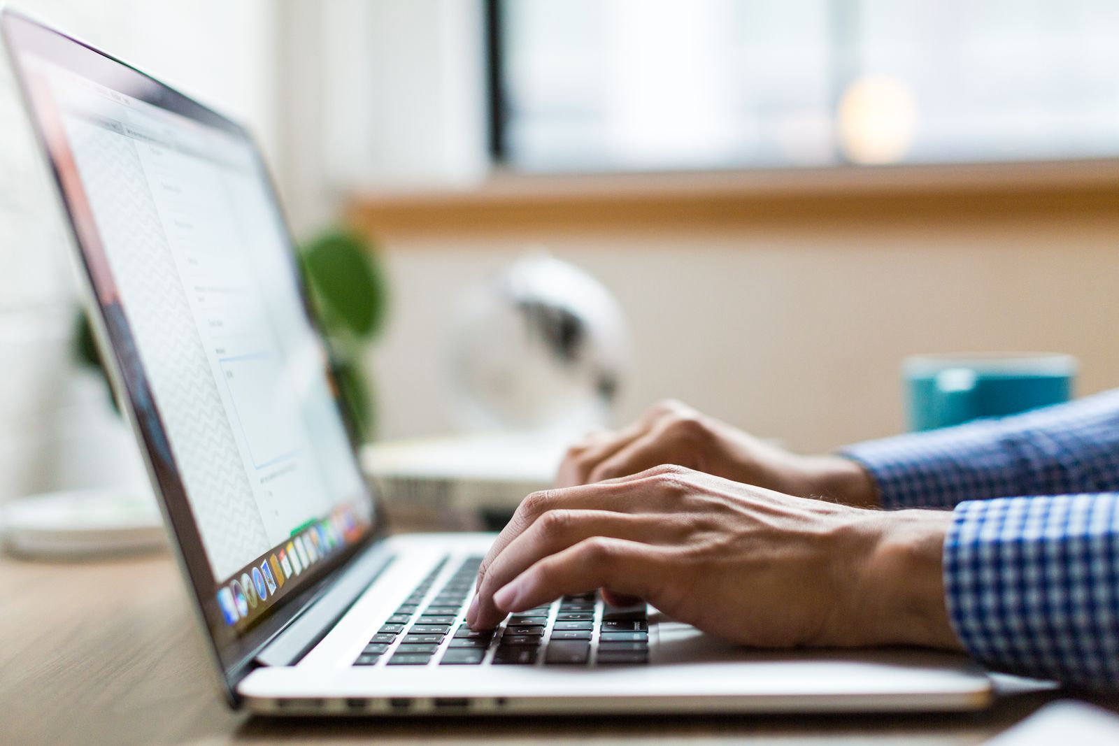 Handen typen een korte zakelijke e-mail op een laptop in een modern kantoor