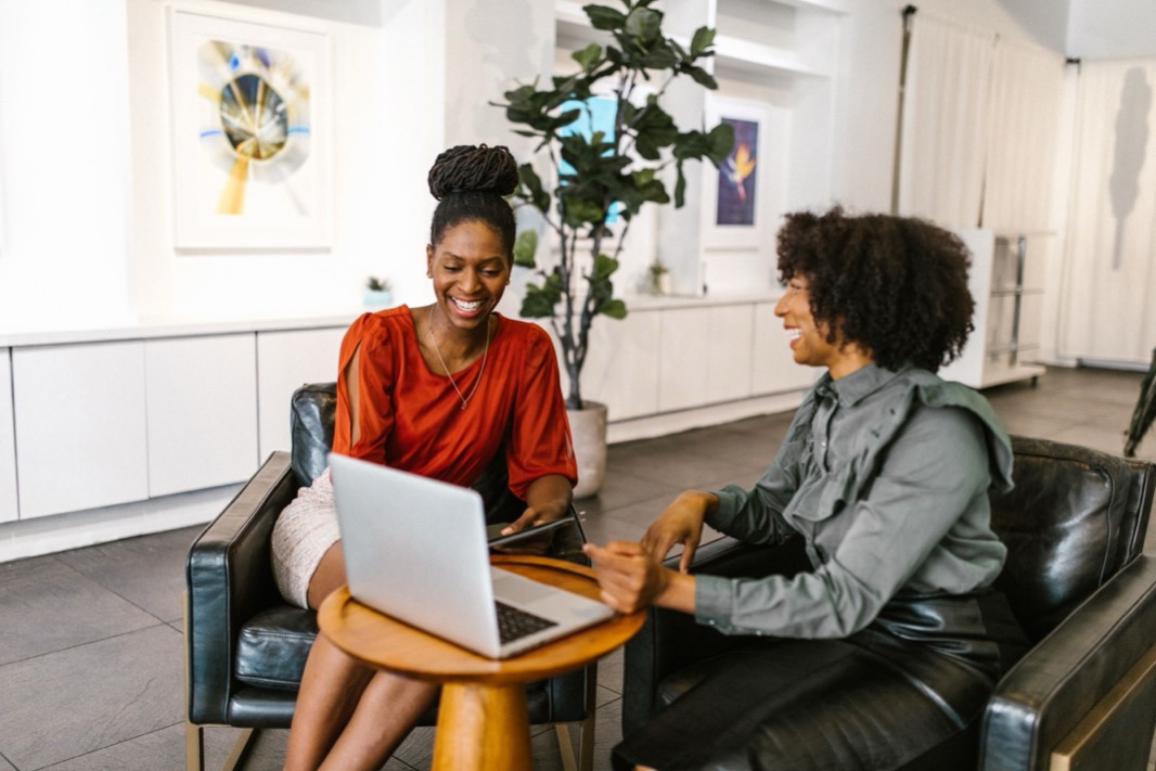 Twee collega's glimlachen terwijl ze samen een e-mail bespreken achter een laptop