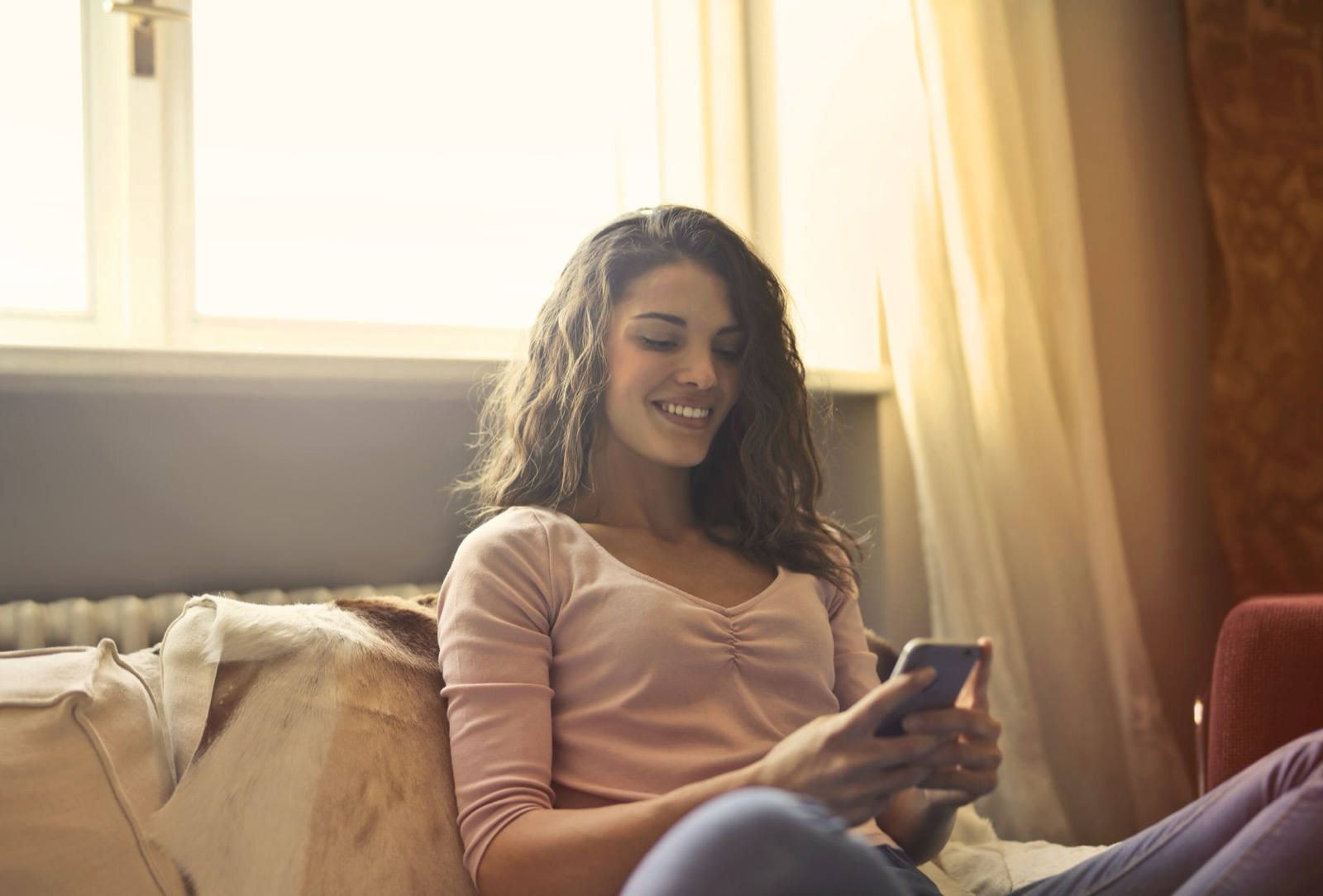 Vrouw zit ontspannen bij het raam en stelt op haar smartphone een vraag aan haar AI-coach over haar gedragsstijl