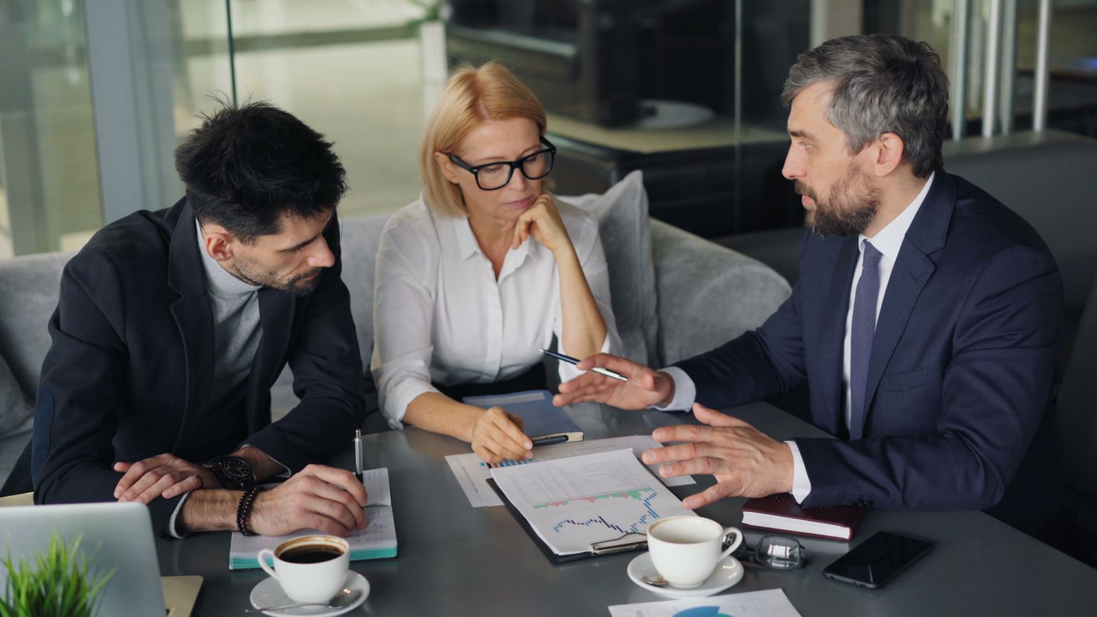 Leidinggevende in gesprek met twee collega's aan een tafel met koffie, als beeld van leidinggeven aan oud-collega's