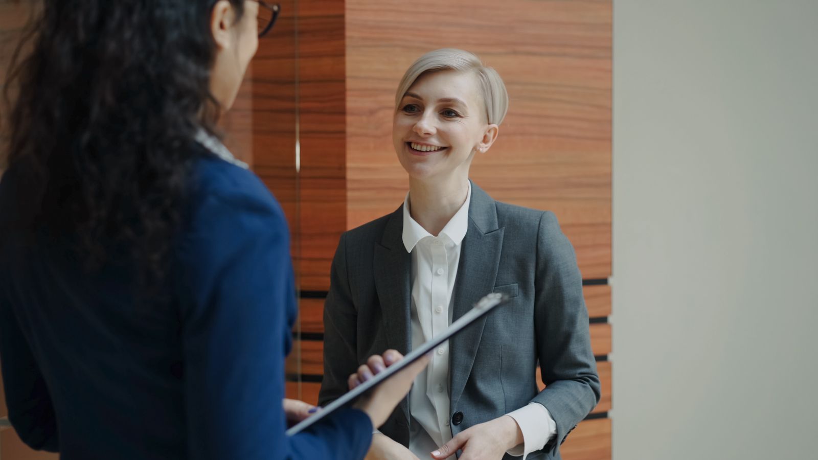 Interviewer met klembord stelt gedragsgerichte interviewvragen aan een glimlachende kandidaat in een sollicitatiegesprek