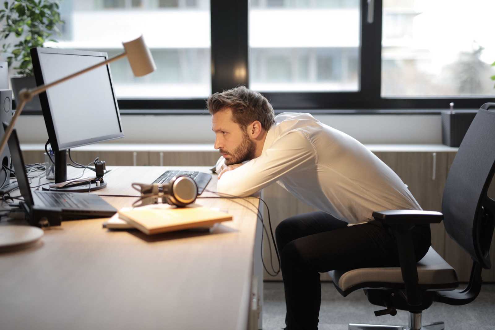 Vermoeide professional achter zijn bureau staart naar het scherm, goed in zijn werk maar niet gemotiveerd