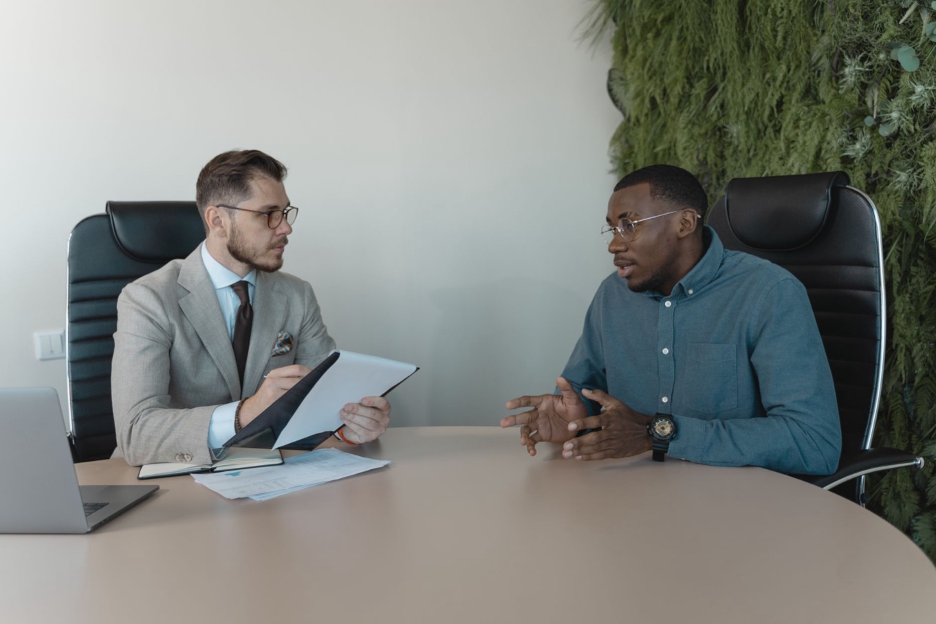 Sollicitatiegesprek aan een ronde tafel: een interviewer met notities luistert naar een kandidaat die over de eigen motivatie vertelt