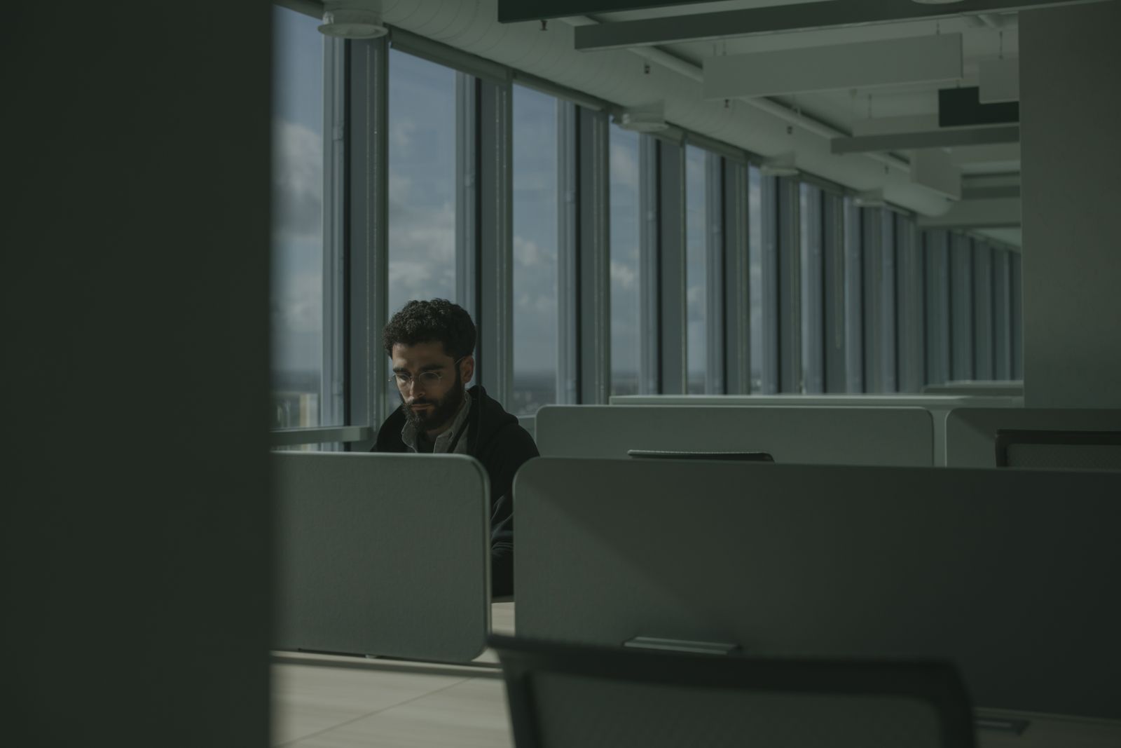 Een collega werkt geconcentreerd en teruggetrokken alleen aan een bureau in een kantoor, beeld bij afstandelijk gedrag en DISC