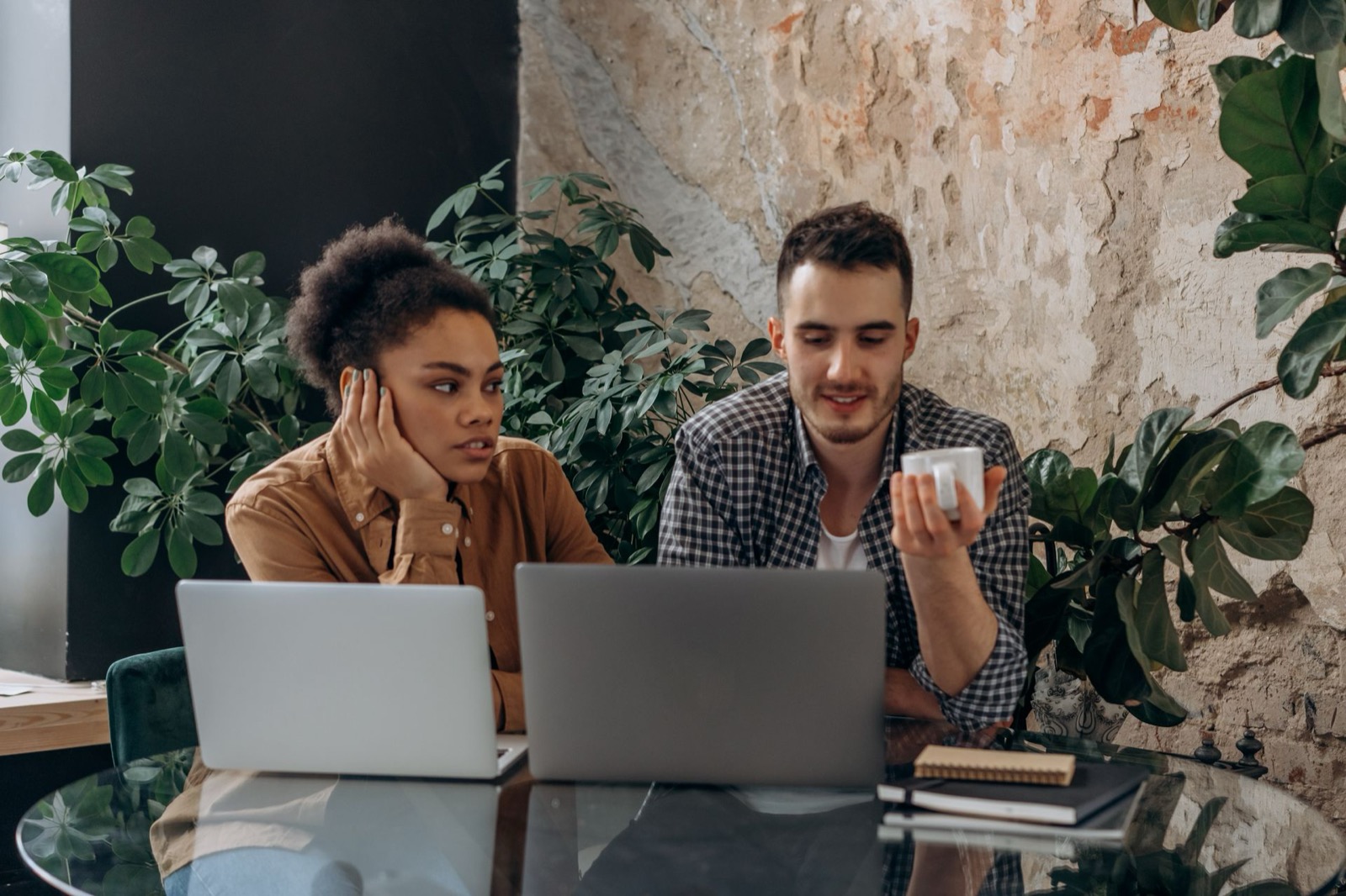 Twee collega's werken samen aan een bureau in een lichte, groene werkruimte, ieder in een eigen werktempo