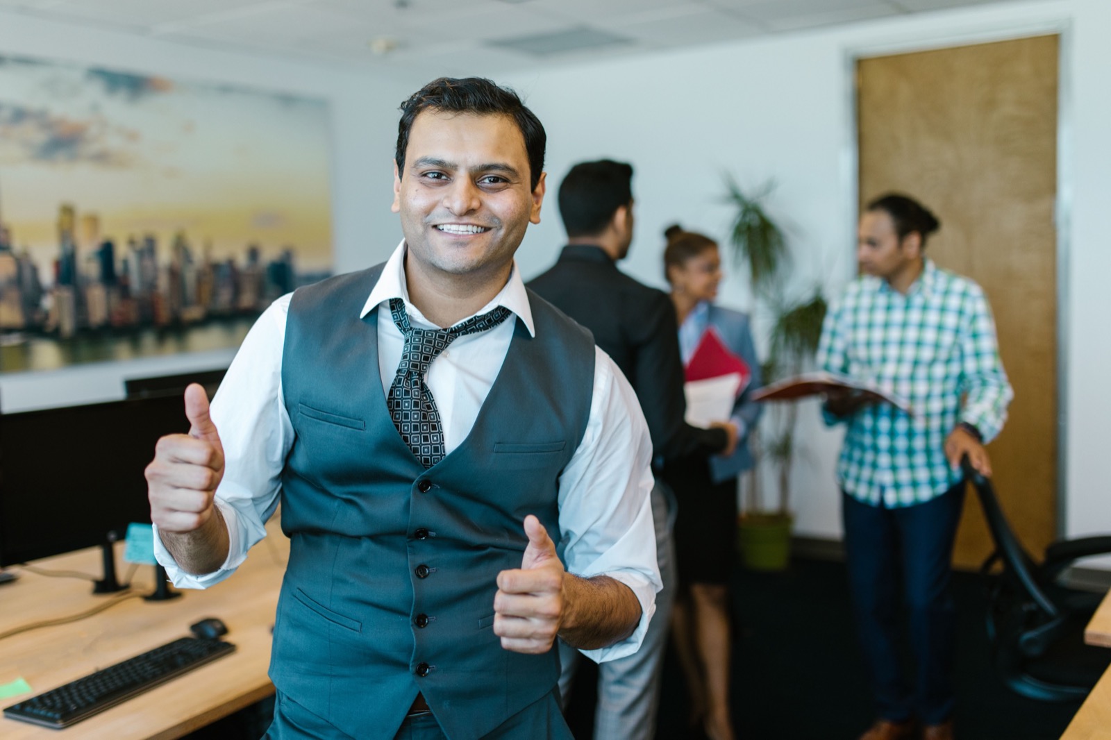 Collega steekt lachend twee duimen op op kantoor, symbool voor een collega die overal ja op zegt
