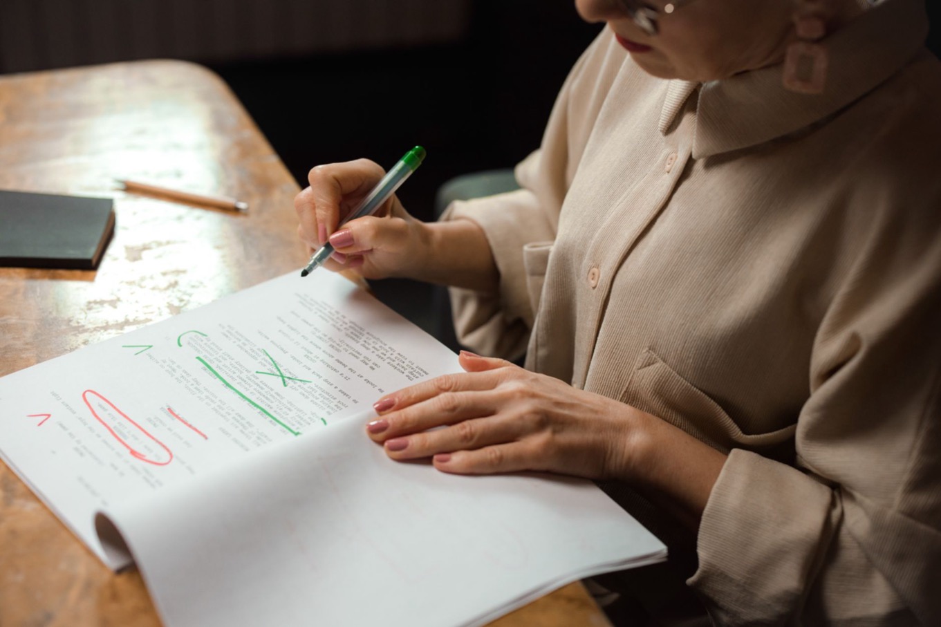 Vrouw corrigeert een document met een groene stift, als beeld voor perfectionisme loslaten op het werk