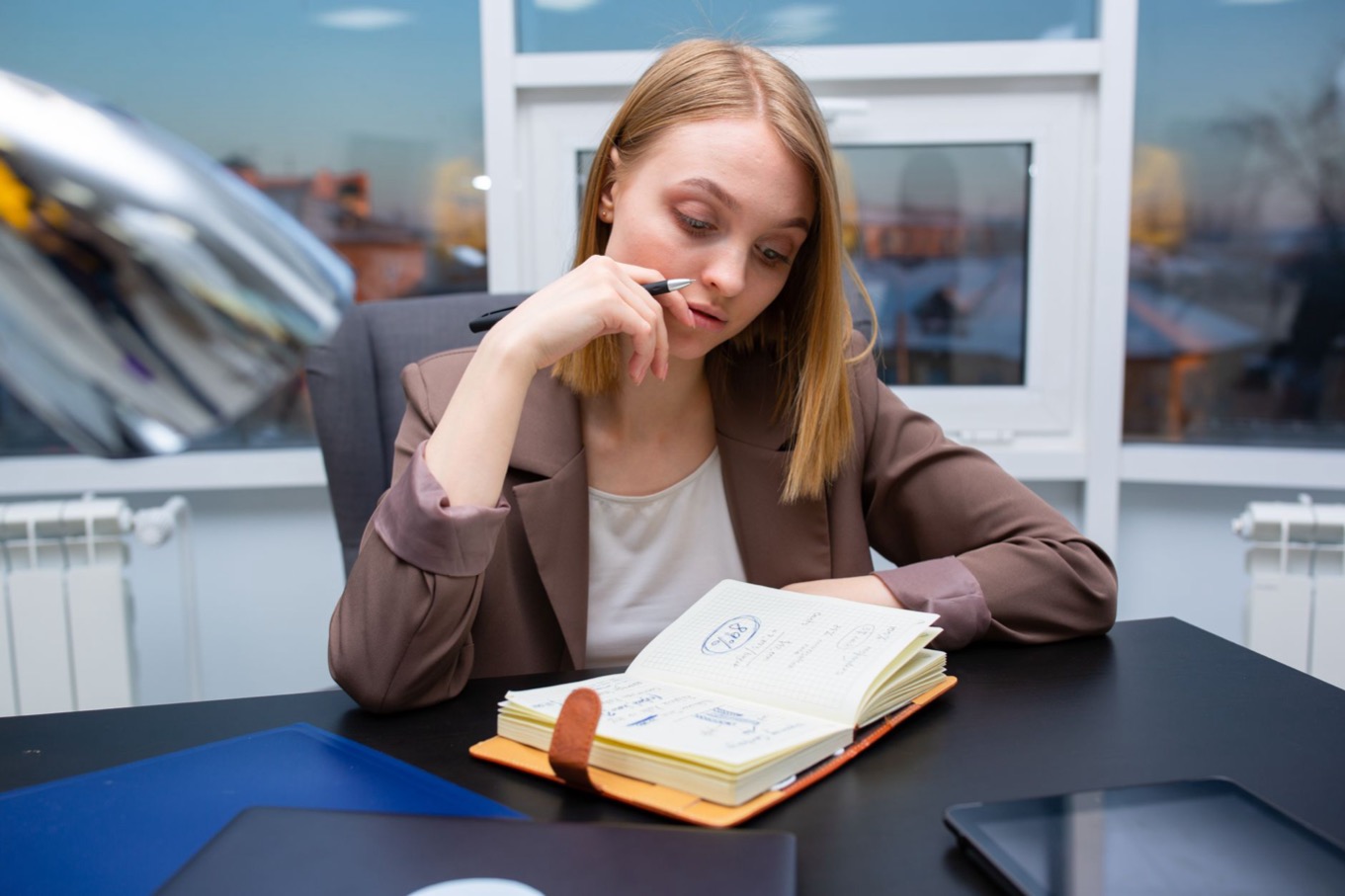 Vrouw aan een bureau denkt na over haar persoonlijk ontwikkelplan en schrijft doelen in een notitieboek