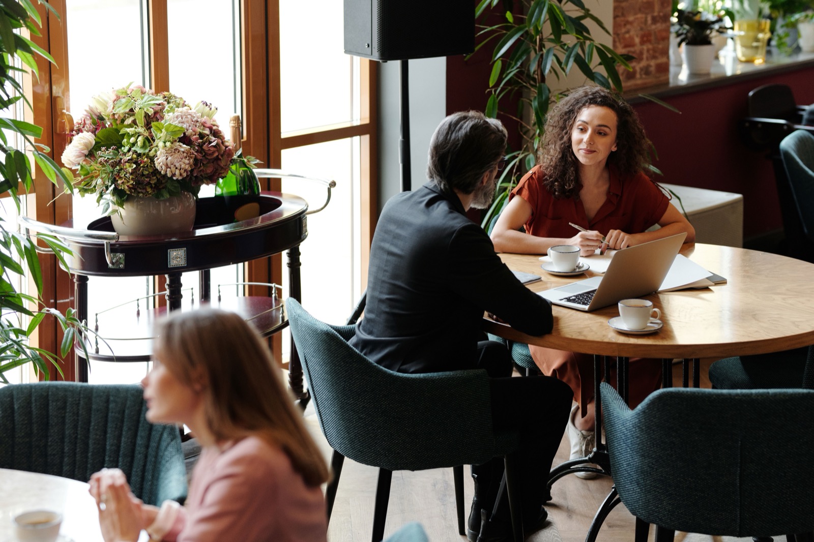 Adviseur en klant in gesprek aan een tafel in een café, met laptop en koffie, tijdens een behoefteanalyse