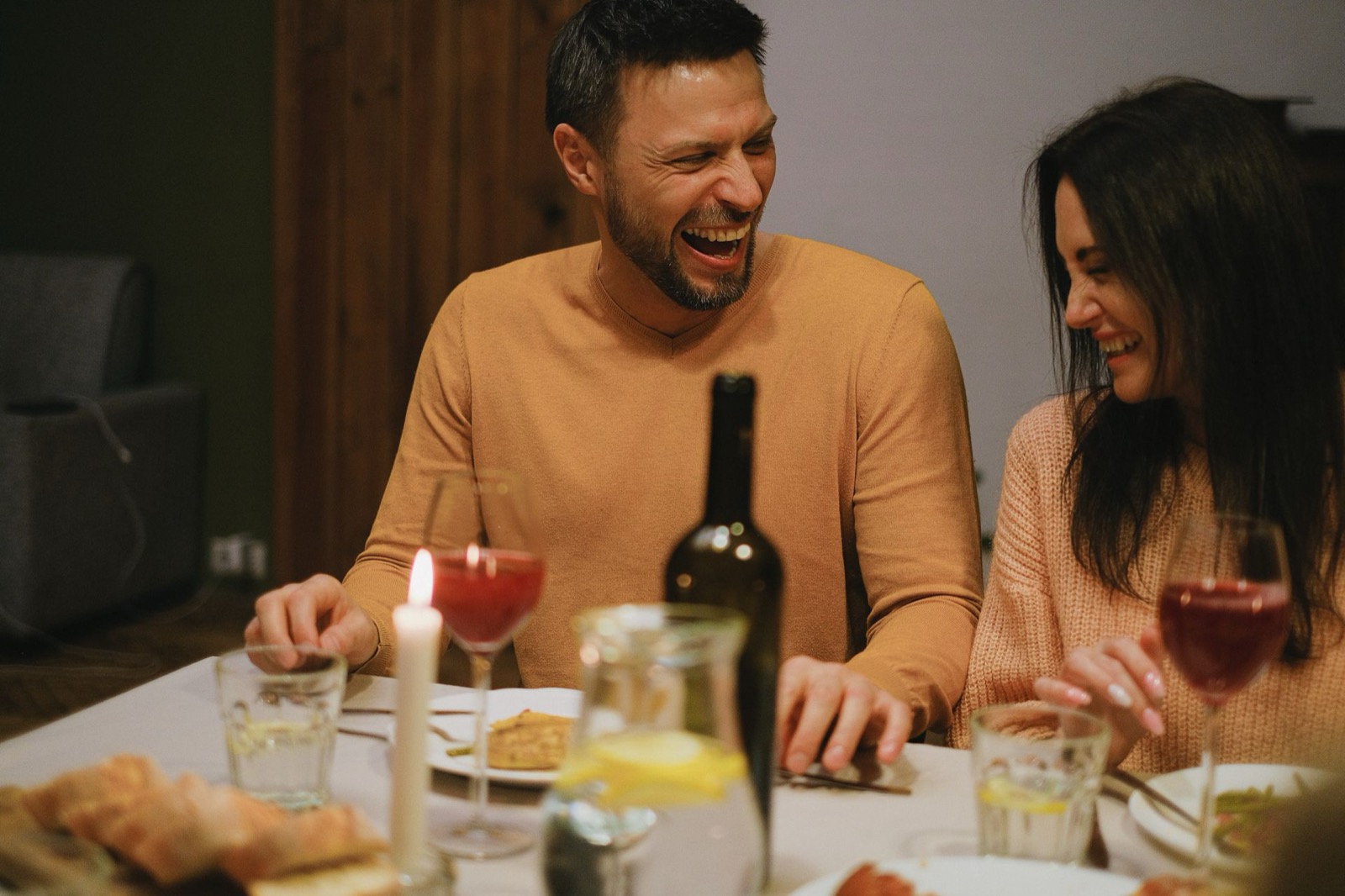 Lachend stel geniet samen van een diner bij kaarslicht, beeld bij partnerkeuze en DISC-kleurcombinaties