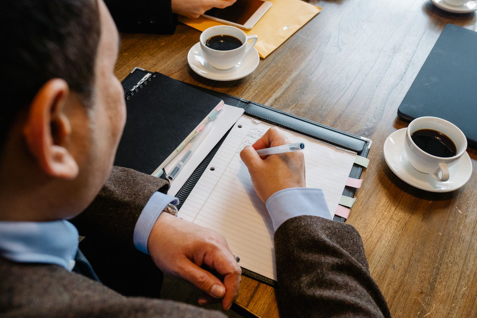 Medewerker maakt aantekeningen in een notitieblok aan tafel met koffie, ter voorbereiding op een jaargesprek