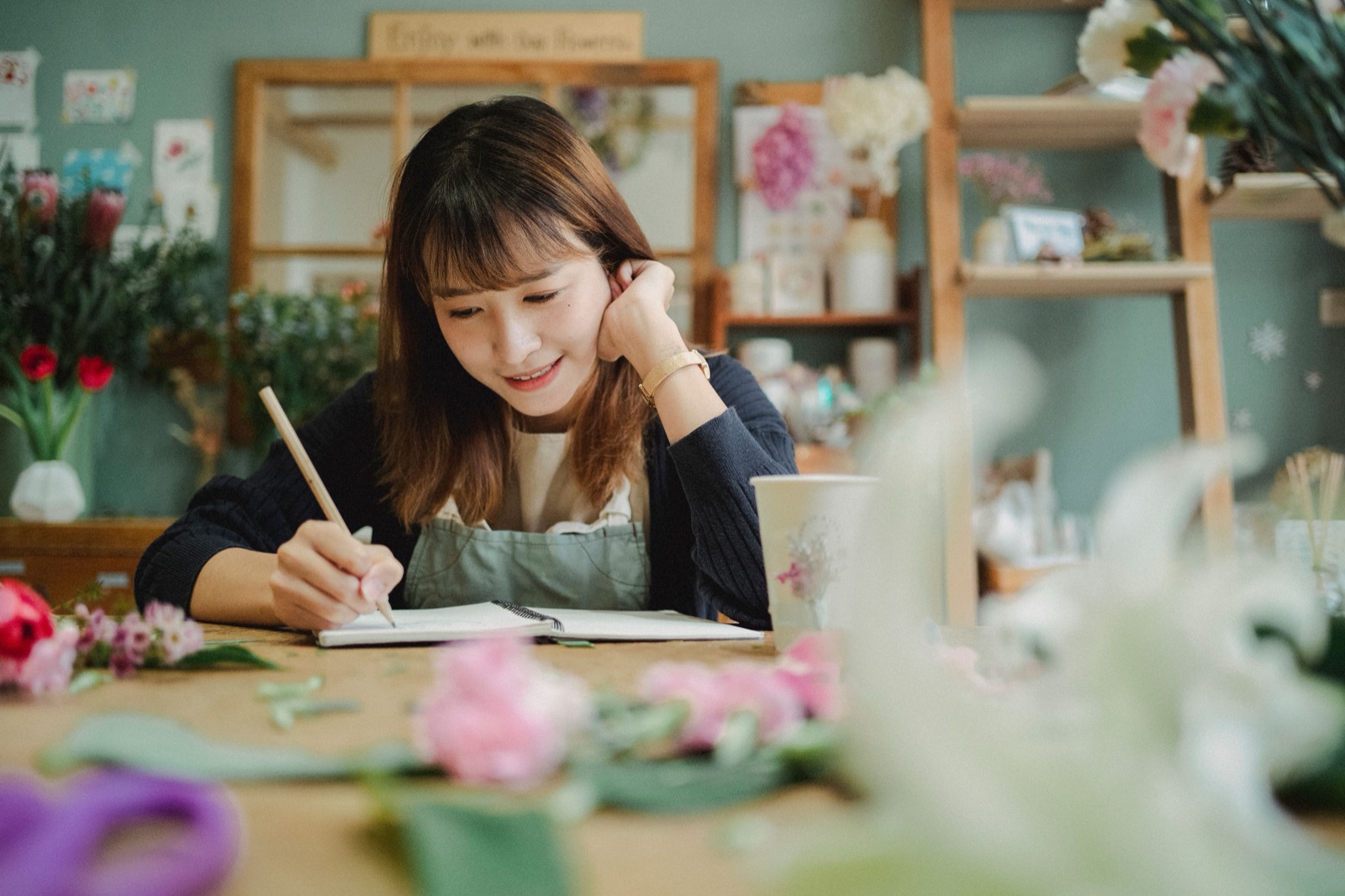 Ondernemer in een eigen bloemenwinkel schrijft glimlachend notities aan de werktafel