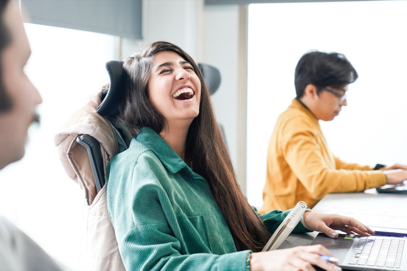 Vrouw lacht energiek achter haar bureau op kantoor, werk dat haar DISC-stijl energie geeft