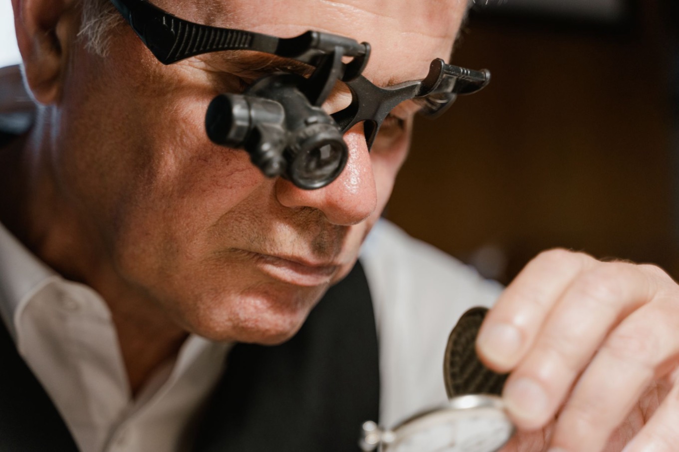 Horlogemaker met loep bekijkt een zakhorloge van dichtbij, beeld bij het Perfectionist-patroon in DISC: oog voor detail en kwaliteit