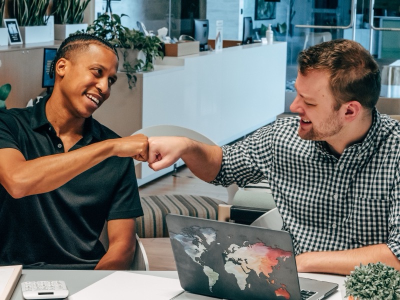 Twee gelijkwaardige collega's geven elkaar een fist bump na een geslaagde samenwerking op kantoor