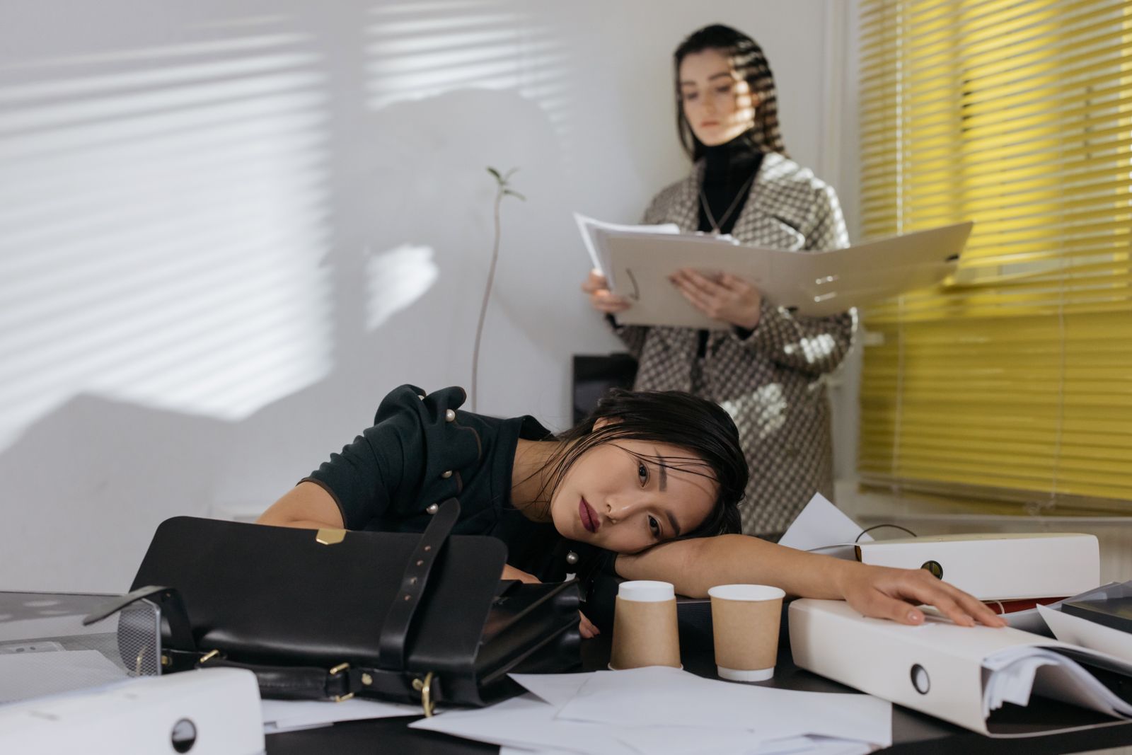 Uitgeputte medewerker rust op het bureau terwijl een collega doorwerkt, als beeld bij energie en duurzame inzetbaarheid