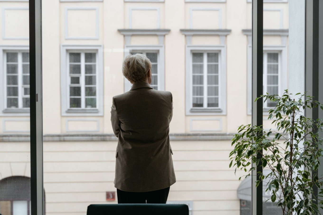 Professional kijkt peinzend uit het kantoorraam, zoals een S-stijl die zich onder stress stil terugtrekt