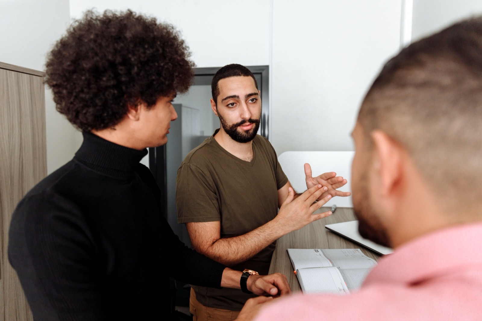 Drie collega's in gesprek op kantoor, een van hen legt iets uit terwijl de anderen luisteren: een informele leider in een team