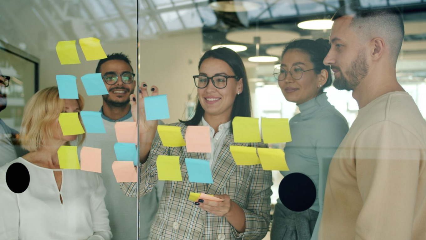 Team maakt samen werkafspraken met gekleurde memoblaadjes op een glazen wand op kantoor