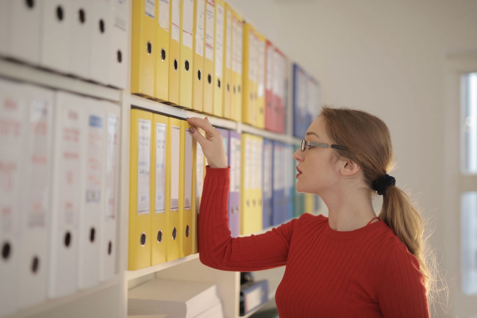Vrouw zoekt in ordners op een kantoorplank, symbool voor DISC-rapporten die ongebruikt op de plank liggen in de organisatie