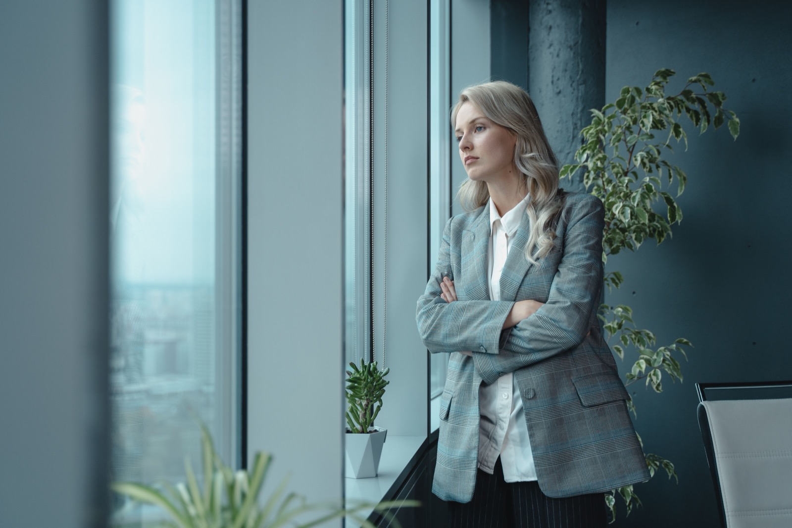 Vrouw in een grijs colbert kijkt peinzend uit een kantoorraam, als beeld bij het verschil tussen gedrag (DISC) en denkvoorkeur (HBDI)