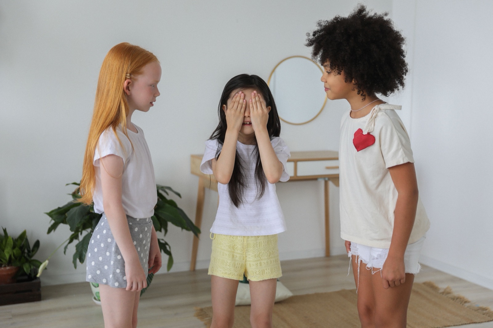 Drie kinderen spelen verstoppertje in een lichte kamer, elk met eigen gedrag: DISC bij kinderen