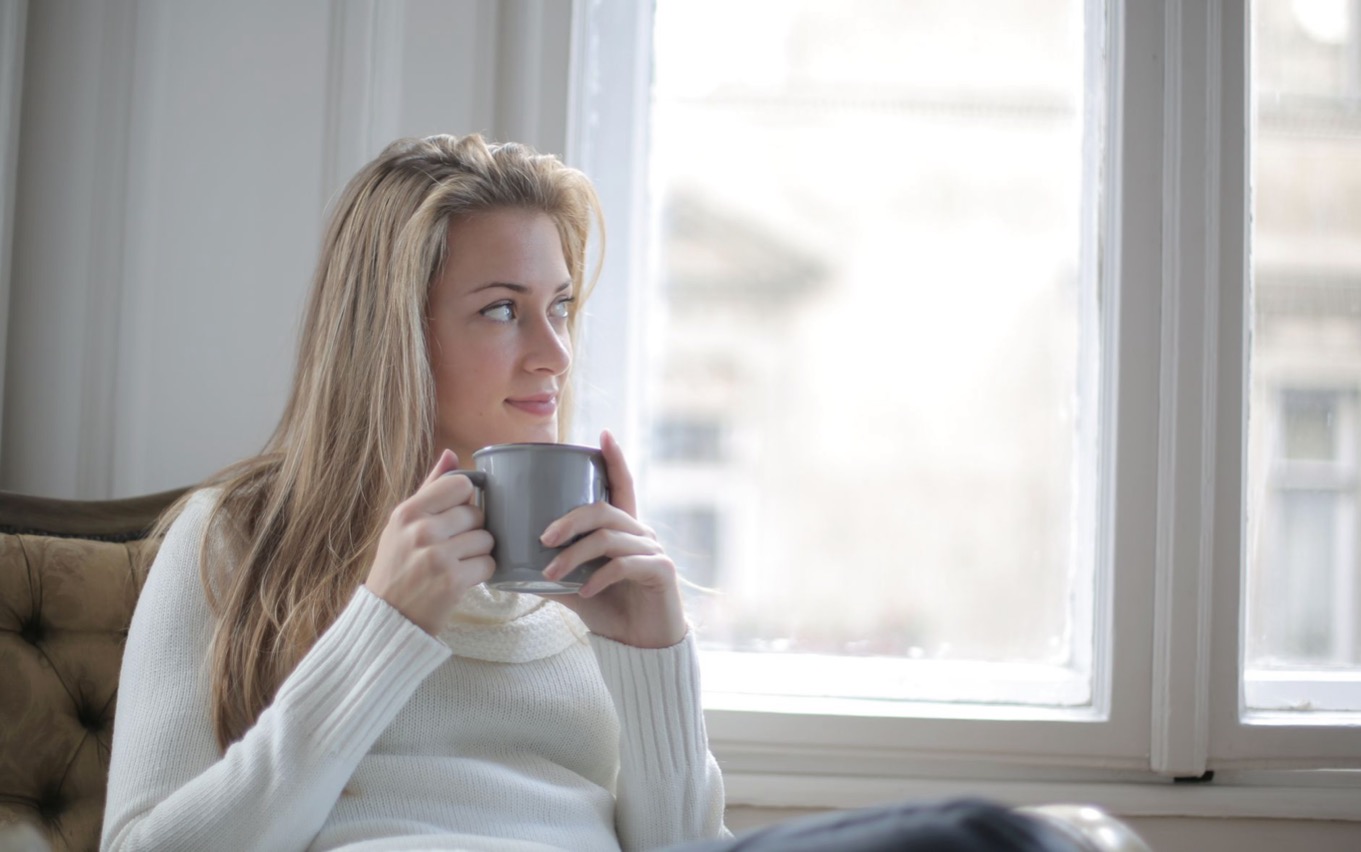 Vrouw geniet van koffie bij een licht raam: energiegevers en energievreters in balans