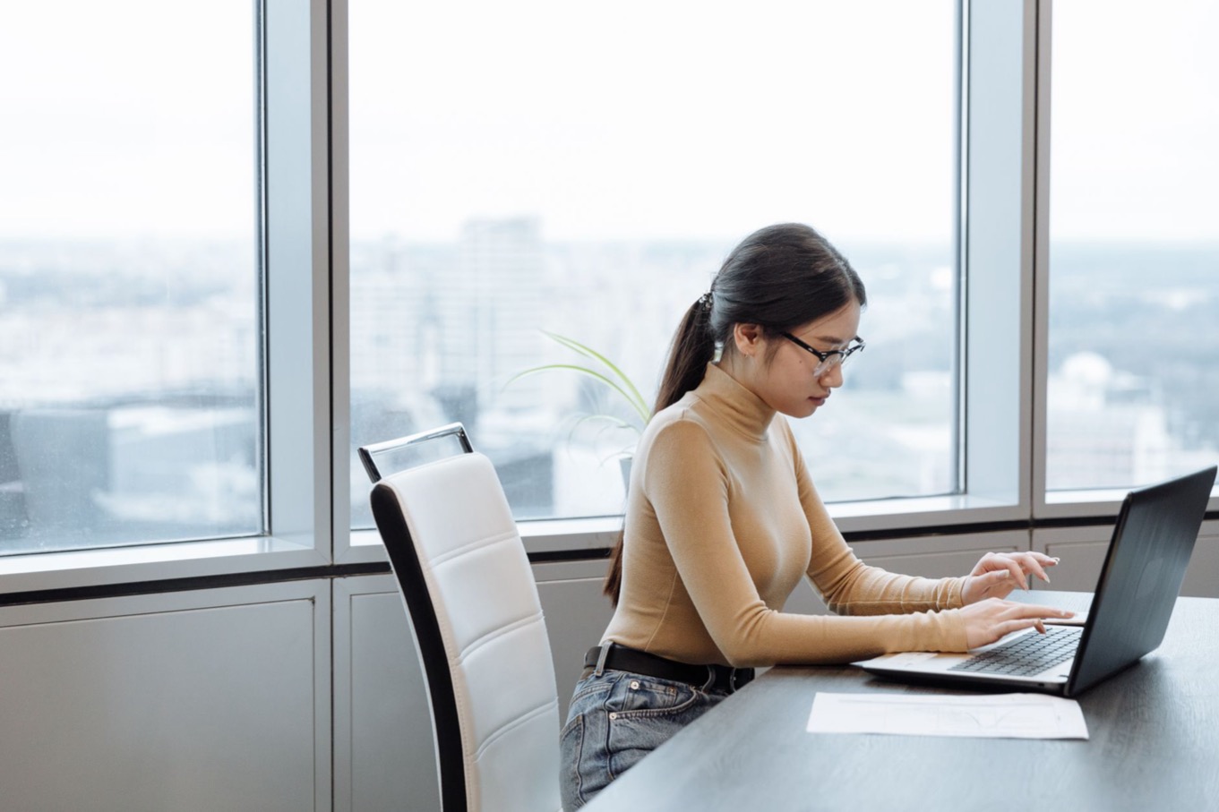 Vrouw werkt geconcentreerd en rustig aan een laptop bij een groot raam op kantoor, als beeld voor introvert zijn op de werkvloer