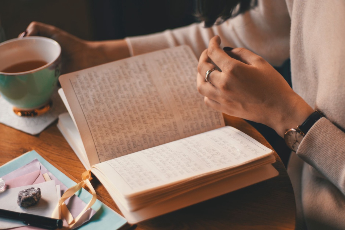 Vrouw schrijft antwoorden op zelfreflectievragen in een notitieboek, met een kop thee op een houten tafel
